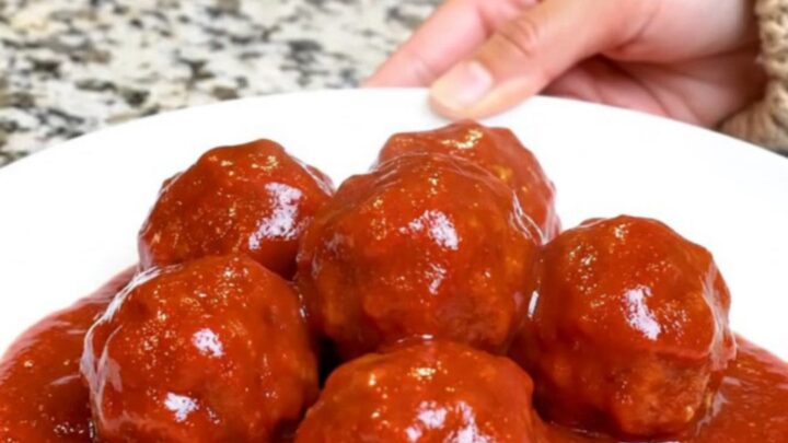A serving spoon lifting saucy turkey meatballs from a black slow cooker insert.