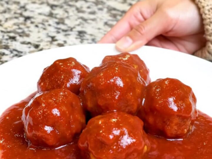 A serving spoon lifting saucy turkey meatballs from a black slow cooker insert.
