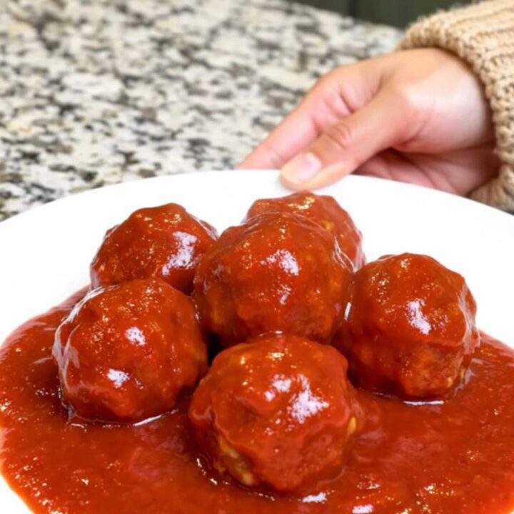 A serving spoon lifting saucy turkey meatballs from a black slow cooker insert.