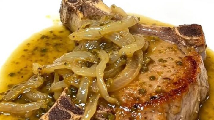 A close-up of tender, slow-cooked pork chops covered in a rich chili lime sauce and soft red onions on a white plate.