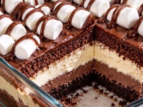 A glass casserole dish filled with layered crumb crust, pudding, cream, cake, and marshmallows drizzled with ganache.