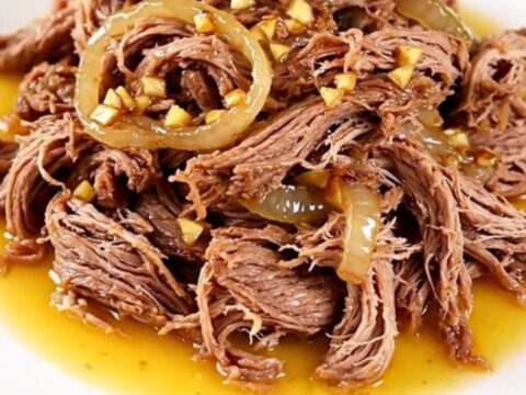 A high-angle shot of a raw beef chuck roast in a black slow cooker with onions and citrus juice.