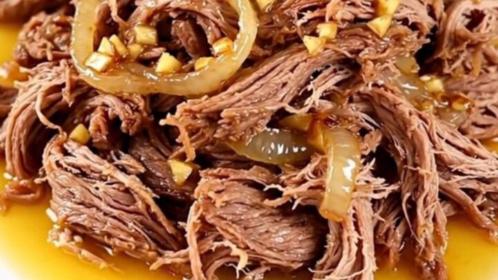 A high-angle shot of a raw beef chuck roast in a black slow cooker with onions and citrus juice.