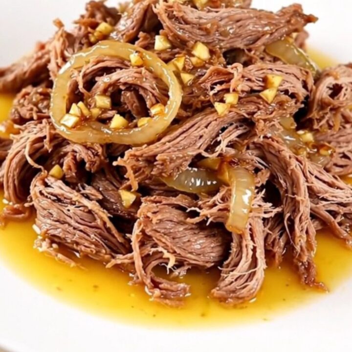 A high-angle shot of a raw beef chuck roast in a black slow cooker with onions and citrus juice.