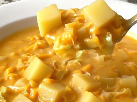 A top-down view of a black slow cooker filled with raw potato cubes, chopped cabbage, and onions, ready to be cooked.
