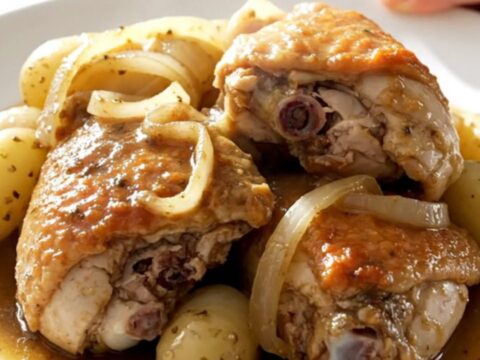 A top-down view of slow-cooked chicken thighs with tender potatoes and onions in a savory broth inside a black slow cooker.