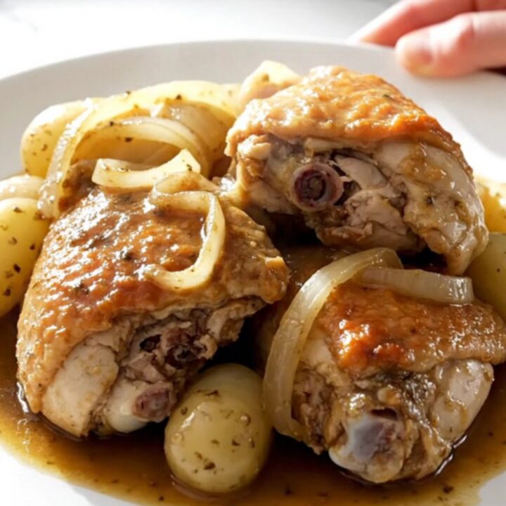 A top-down view of slow-cooked chicken thighs with tender potatoes and onions in a savory broth inside a black slow cooker.