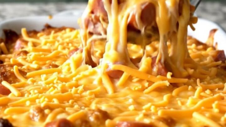 A top-down view of a rectangular baking dish filled with elbow macaroni, hot dog coins, and cheddar sauce.