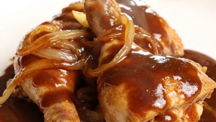 A high-angle shot of raw chicken leg quarters and sliced onions in a slow cooker insert before cooking.