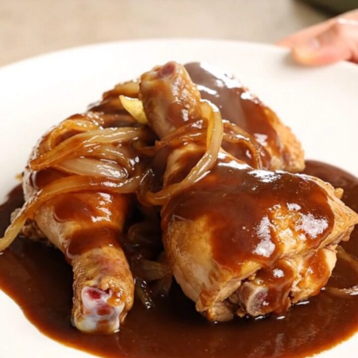 A high-angle shot of raw chicken leg quarters and sliced onions in a slow cooker insert before cooking.