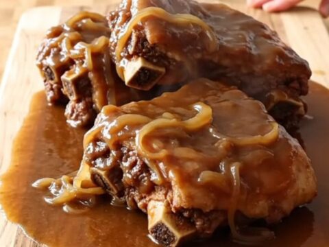 A rustic presentation of slow-cooked spareribs coated in a rich, thick brown onion gravy on a wooden board.