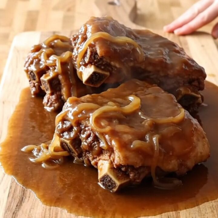 A rustic presentation of slow-cooked spareribs coated in a rich, thick brown onion gravy on a wooden board.