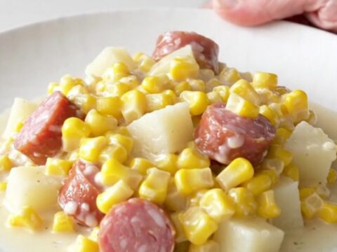A close-up of a bowl filled with creamy sausage, tender potato cubes, and sweet creamed corn.