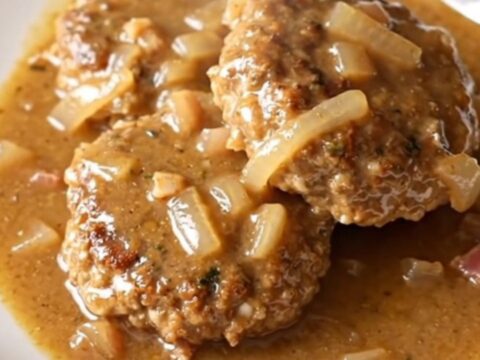 A high-angle shot of cooked turkey patties smothered in a creamy bacon and onion gravy inside a slow cooker.