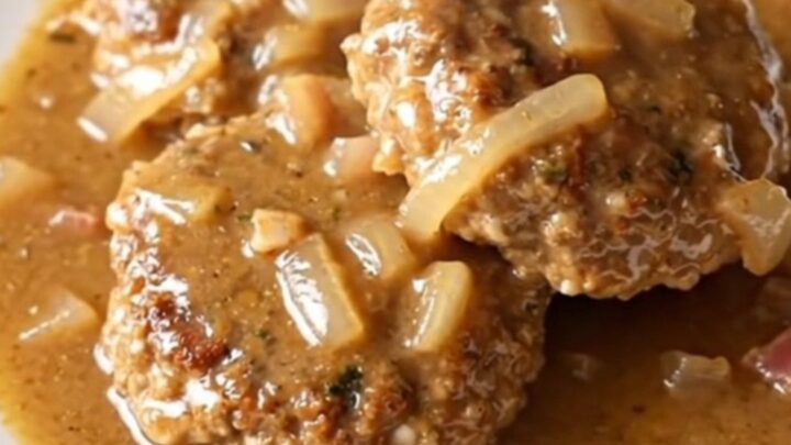 A high-angle shot of cooked turkey patties smothered in a creamy bacon and onion gravy inside a slow cooker.