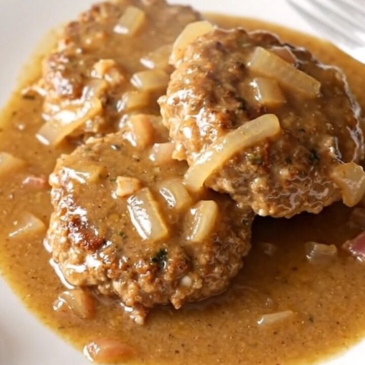 A high-angle shot of cooked turkey patties smothered in a creamy bacon and onion gravy inside a slow cooker.