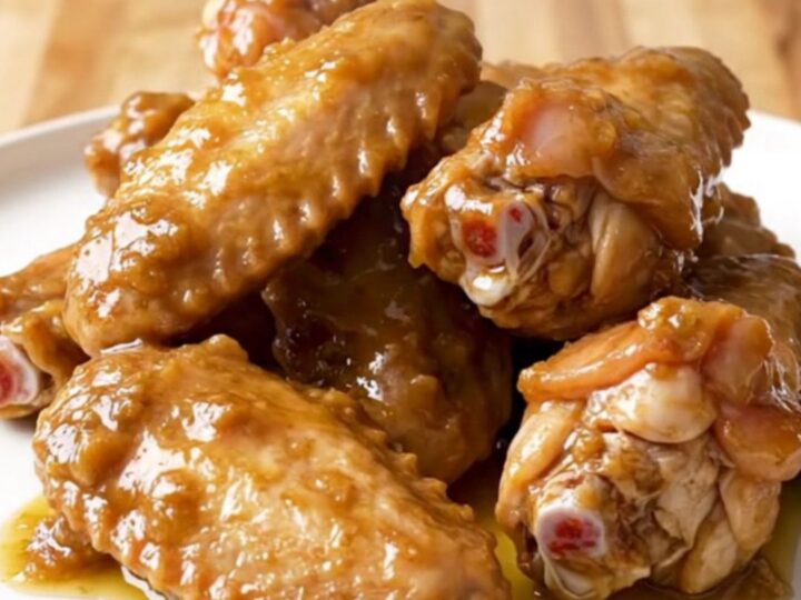 A close-up of tender, slow-cooked chicken wings coated in a rich, buttery, and spiced Chesapeake sauce on a white plate.