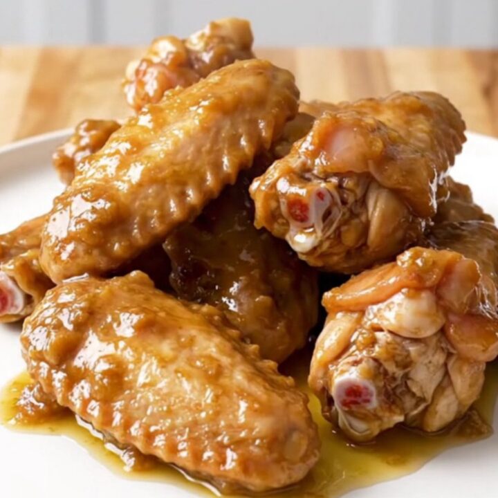 A close-up of tender, slow-cooked chicken wings coated in a rich, buttery, and spiced Chesapeake sauce on a white plate.