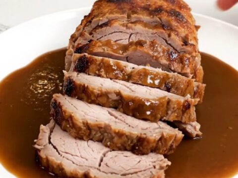 A close-up of a perfectly cooked pork tenderloin sliced into rounds and drizzled with a rich, dark bourbon-infused sauce.