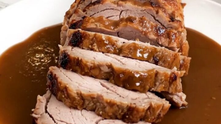 A close-up of a perfectly cooked pork tenderloin sliced into rounds and drizzled with a rich, dark bourbon-infused sauce.