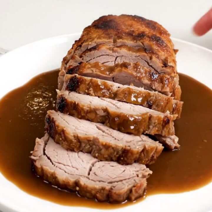 A close-up of a perfectly cooked pork tenderloin sliced into rounds and drizzled with a rich, dark bourbon-infused sauce.