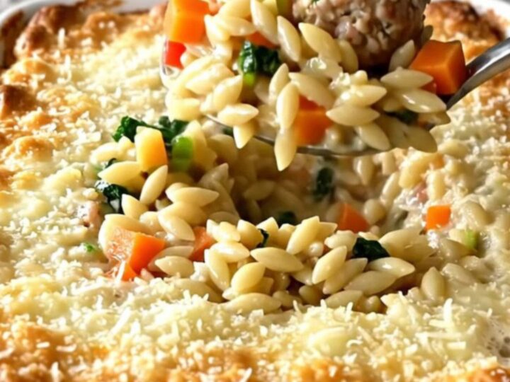 A rectangular baking dish filled with a golden, cheesy Italian wedding orzo bake on a speckled granite countertop.