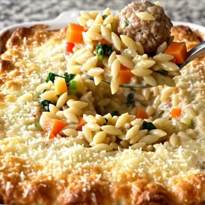 A rectangular baking dish filled with a golden, cheesy Italian wedding orzo bake on a speckled granite countertop.