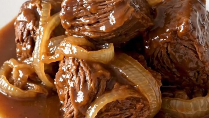 A rustic slow cooker pot roast served on a white plate with soft onions and dark, rich gravy.