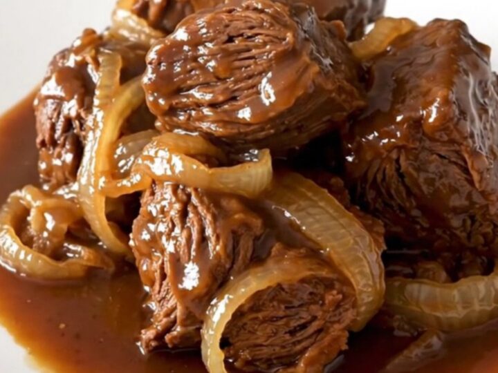 A rustic slow cooker pot roast served on a white plate with soft onions and dark, rich gravy.