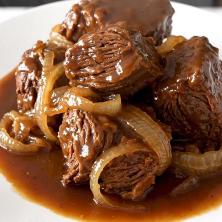 A rustic slow cooker pot roast served on a white plate with soft onions and dark, rich gravy.
