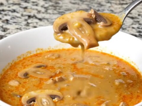 A steaming bowl of creamy Hungarian mushroom soup garnished with fresh herbs in a bright, modern kitchen.