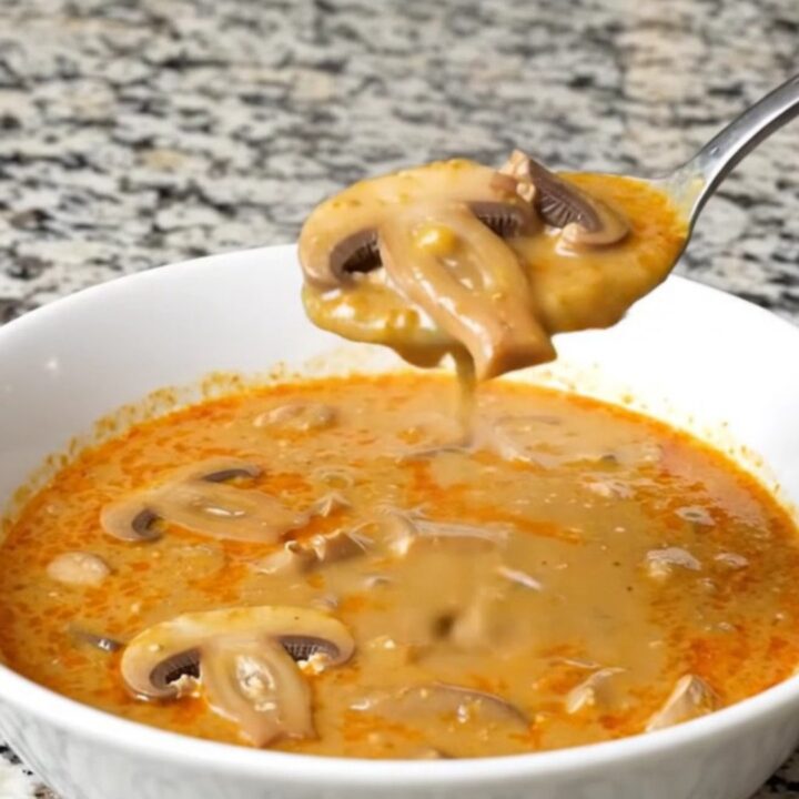 A steaming bowl of creamy Hungarian mushroom soup garnished with fresh herbs in a bright, modern kitchen.