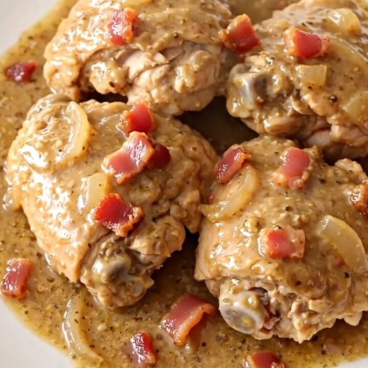 A high-angle shot of tender chicken thighs in a creamy bacon and onion gravy inside a slow cooker.
