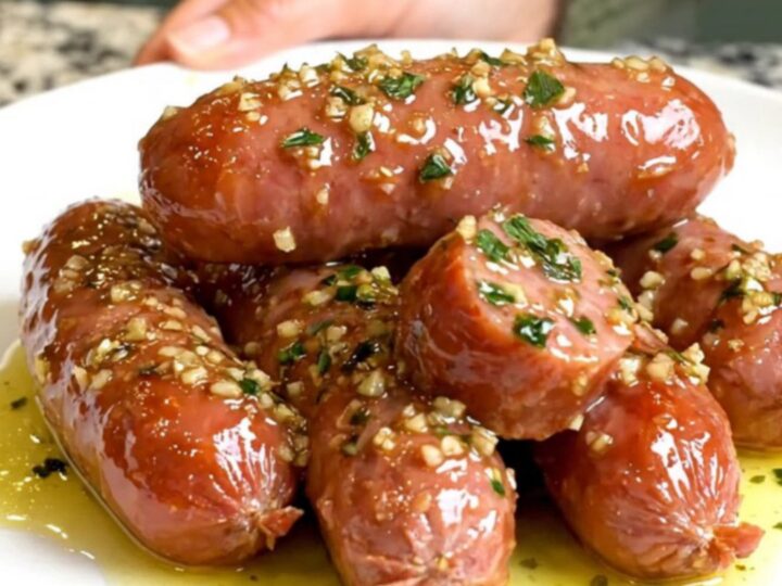 A black slow cooker filled with sliced kielbasa coins coated in a glistening garlic butter sauce.