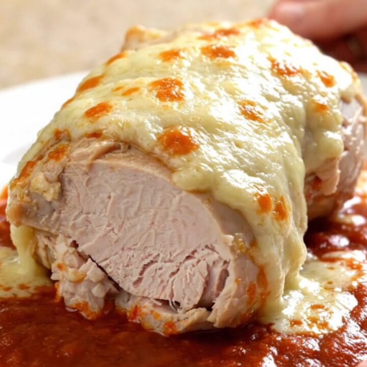 A close-up of tender, slow-cooked turkey breast topped with melted mozzarella and marinara sauce on a white plate.