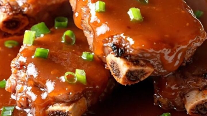 A slow cooker filled with raw pork spareribs being seasoned with green onions and sweet chili sauce.