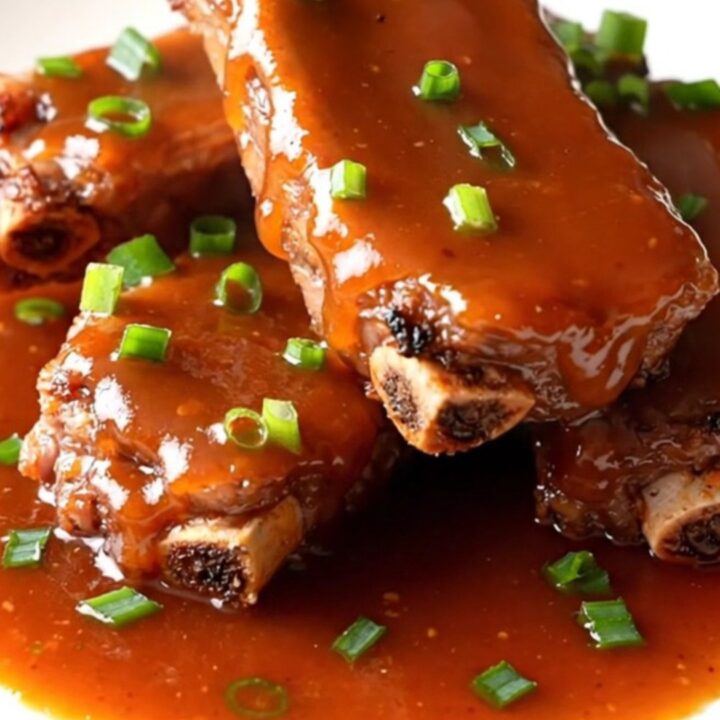 A slow cooker filled with raw pork spareribs being seasoned with green onions and sweet chili sauce.