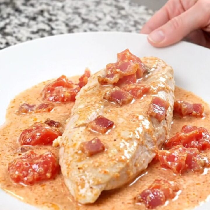 A plate of creamy BLT slow cooker chicken served with a rich, white sauce and bacon crumbles.