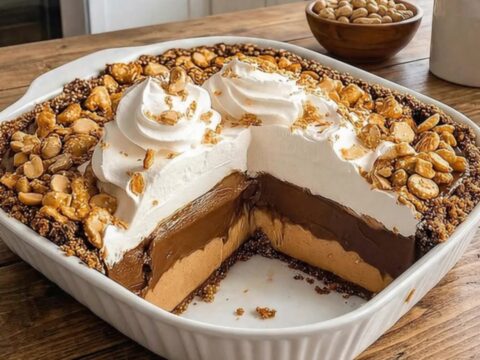 A dessert fork slicing through plush whipped cream, chocolate ganache, and peanut butter pie on a pretzel crust.