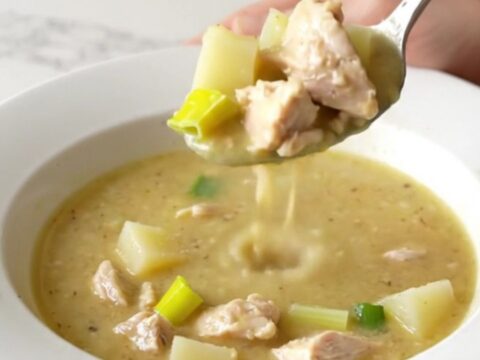 A white bowl filled with creamy chicken, leek, and potato soup, garnished with a sprig of fresh thyme.
