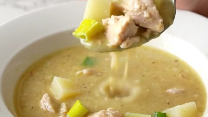 A white bowl filled with creamy chicken, leek, and potato soup, garnished with a sprig of fresh thyme.
