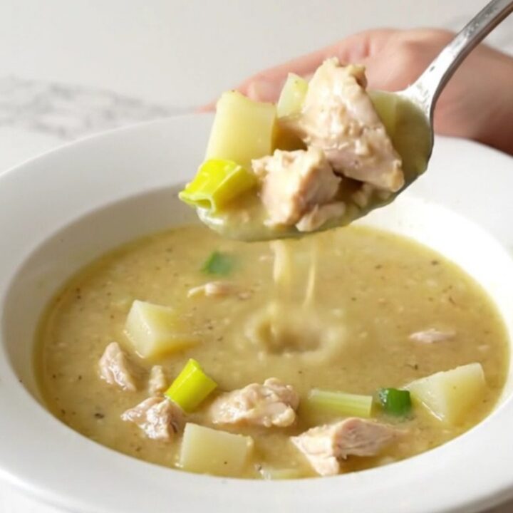 A white bowl filled with creamy chicken, leek, and potato soup, garnished with a sprig of fresh thyme.