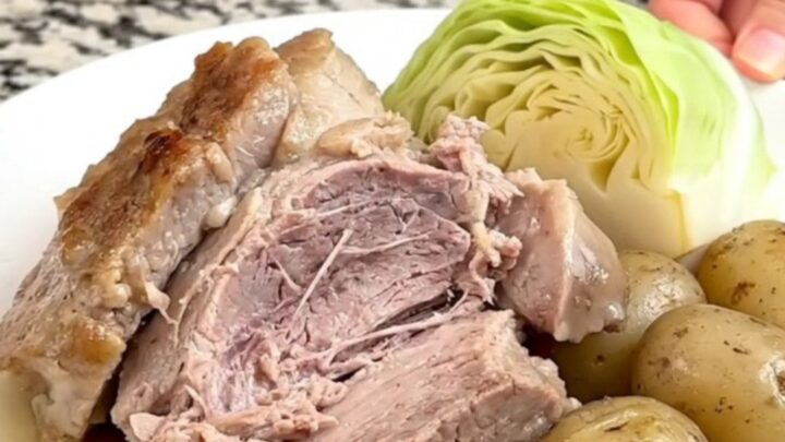 A slow cooker filled with a pork roast, cabbage wedges, and baby potatoes in a savory broth.