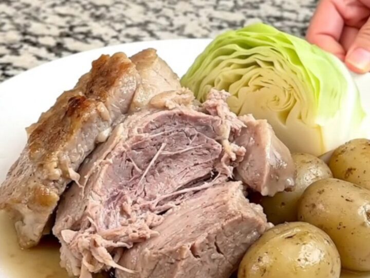 A slow cooker filled with a pork roast, cabbage wedges, and baby potatoes in a savory broth.