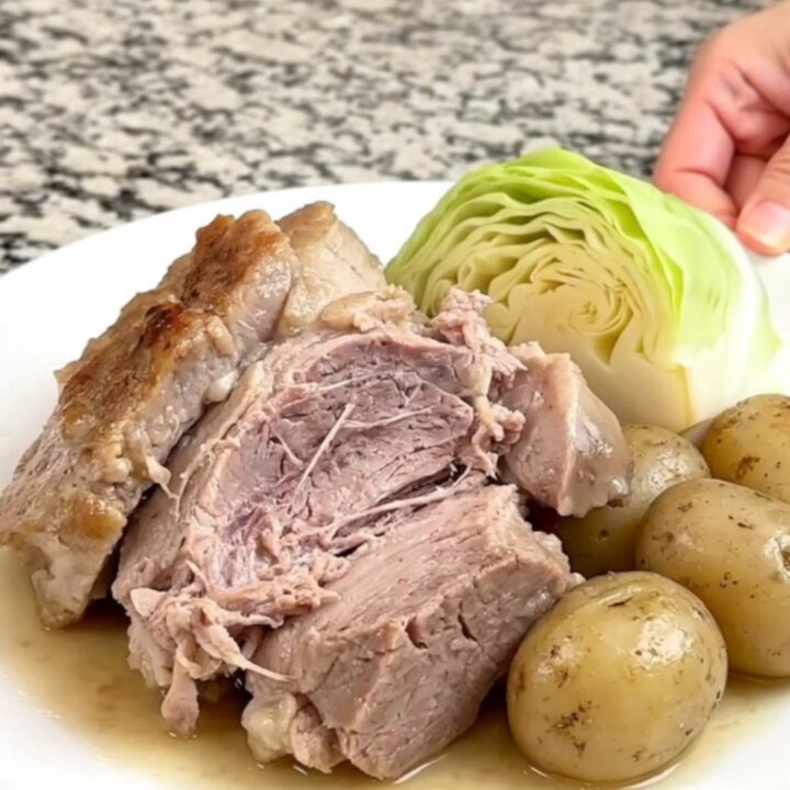 A slow cooker filled with a pork roast, cabbage wedges, and baby potatoes in a savory broth.