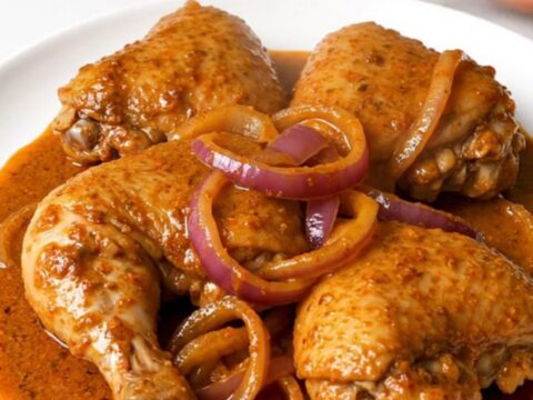 A slow cooker filled with tender chicken thighs, red onion slices, and a vibrant, brick-red achiote sauce.