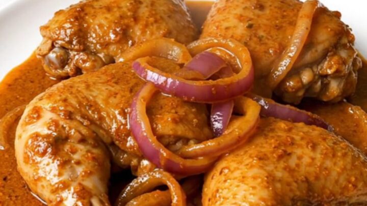 A slow cooker filled with tender chicken thighs, red onion slices, and a vibrant, brick-red achiote sauce.