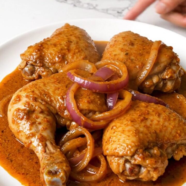 A slow cooker filled with tender chicken thighs, red onion slices, and a vibrant, brick-red achiote sauce.