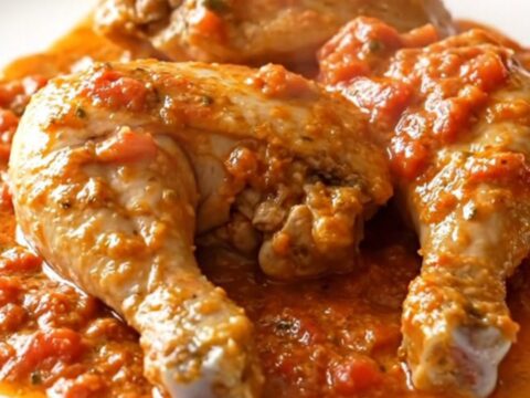 Close-up of creamy tomato feta chicken served in a black slow cooker with a spoon lifting a piece of chicken.