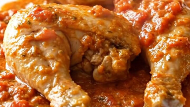 Close-up of creamy tomato feta chicken served in a black slow cooker with a spoon lifting a piece of chicken.